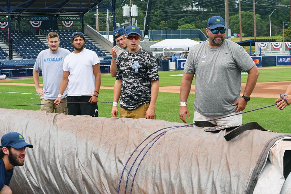 Wildcat baseball team members, along with head coach Howard, right, prepare to pull the tarp over the infield at BB&T Ballpark at Historic Bowman Field, which is transformed for a day into a Major League stadium. Standing, from left, are Brandon Barnyak, Cody Nelson, Trevor Dolin and Conner Curran. At bottom of frame is Joe Gaumer.
