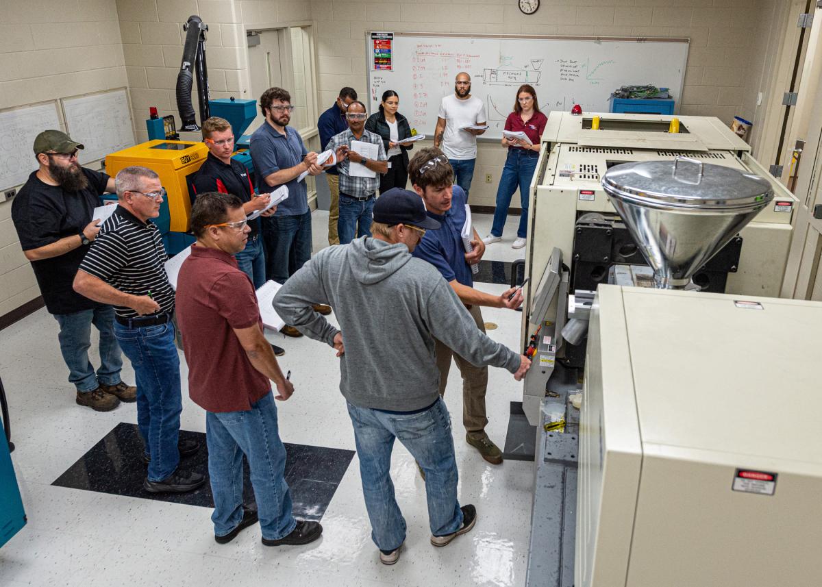 Industry professionals receive hands-on instruction from Mark A. Sneidman (foreground, in blue shirt, gesturing with pen), a member of Pennsylvania College of Technology’s plastics & polymer faculty, during the recent Injection Molding Processing Series workshop hosted by the institution’s Plastics Innovation & Resource Center. 