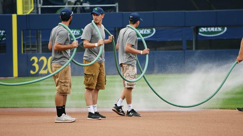  Wildcats lend a hand as the grounds crew waters the infield to keep dust down. From left: Remington Spoonhour,  Brandon Barnyak and Devon Sanders.