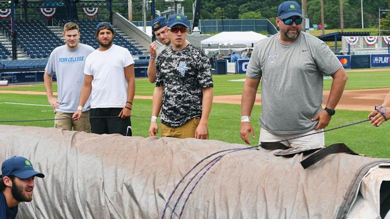  Wildcat baseball team members, along with head coach Chris Howard, right, prepare to pull the tarp over the infield at BB&T Ballpark at Historic Bowman Field, which is transformed for a day into a Major League stadium. Standing, from left, are Brandon Barnyak, Cody Nelson, Trevor Dolin and Conner Curran. At bottom of frame is Joe Gaumer.