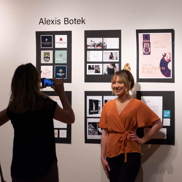 Student displaying work in gallery getting her photo taken